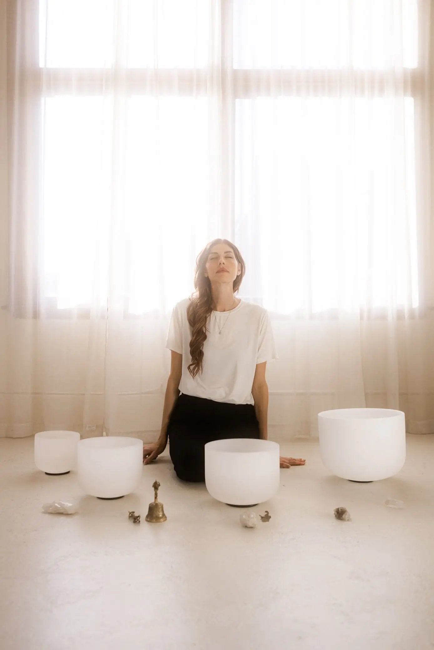 Kasia sitting in a room with large windows, surrounded by singing bowls.