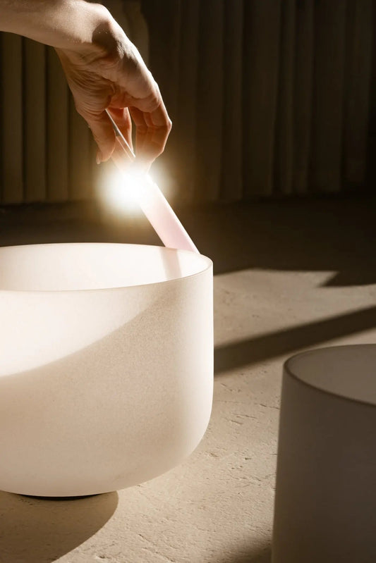 Hand playing sound bowl, white bowl on a wooden surface.